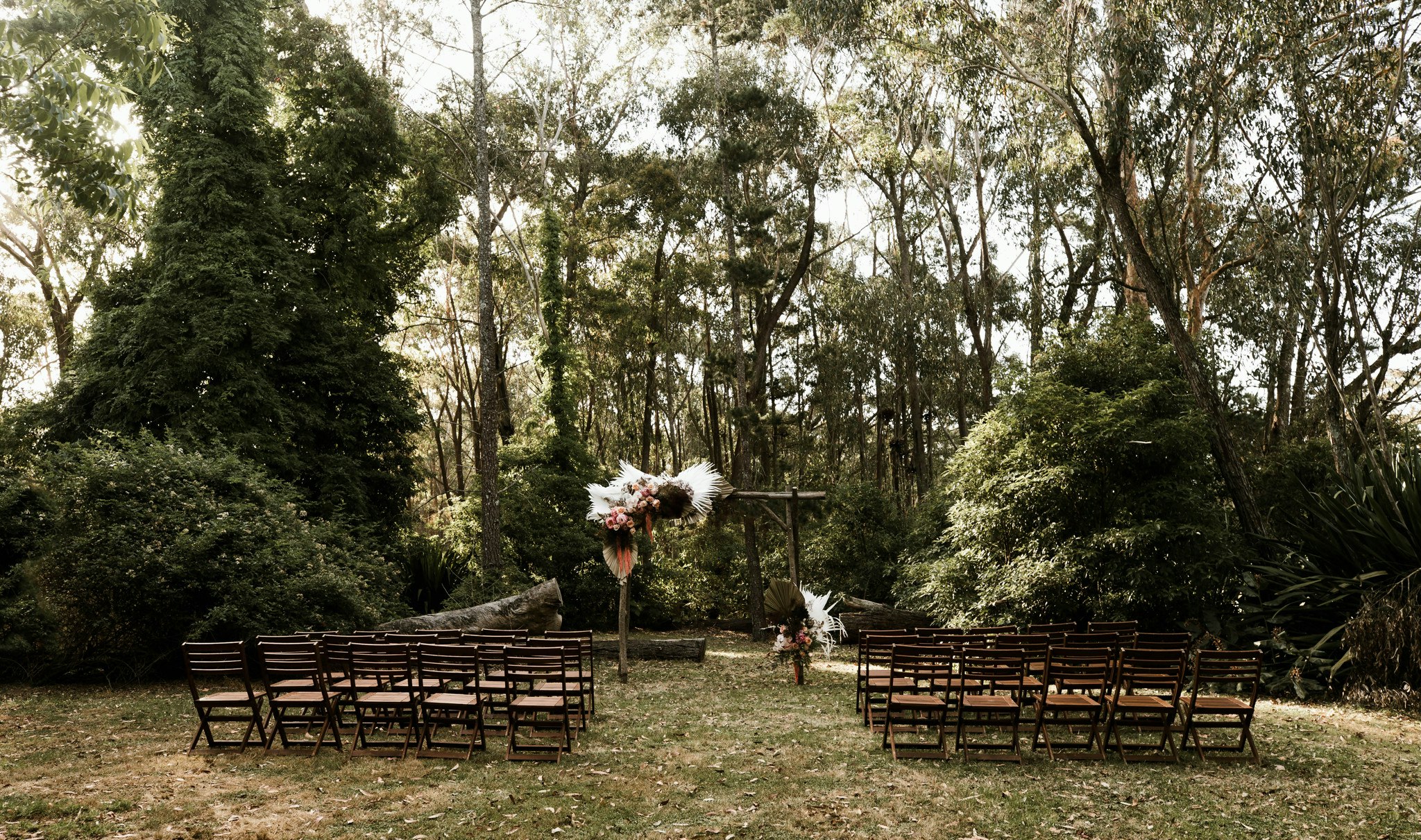 Outdoor wedding ceremony, with wooden archway and seating set amongst lush bushland.